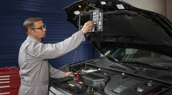 Automotive mechanic using an oscilloscope to compare transmission and engine module communication signals.
